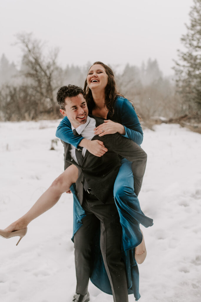 engaged couple doing a piggyback ride in the snow