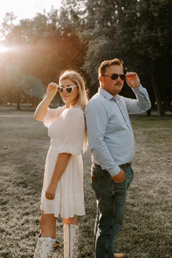 engaged couple standing back to back with sunglasses on