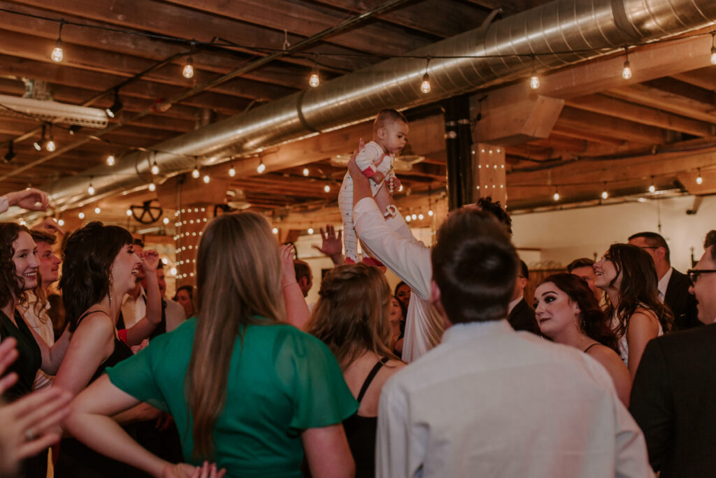 baby being held up on the dance floor during the wedding reception