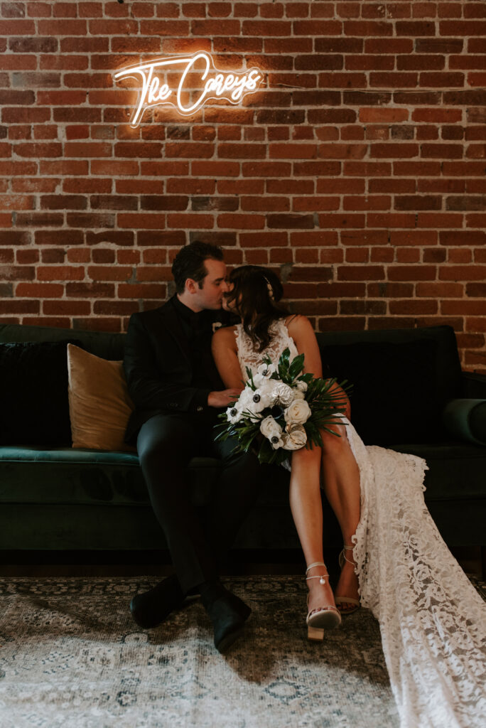 Bride and groom kissing on the couch in front of a neon sign