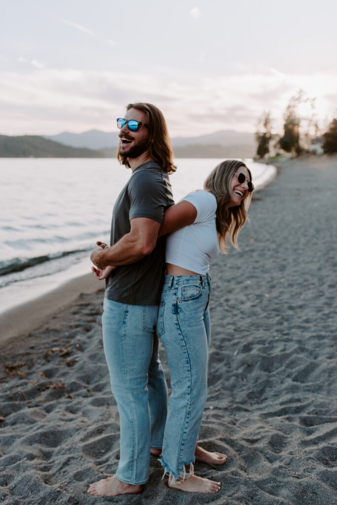 Couple with sunglasses holding hands and laughing on the beach at Lake Coeur D'Alene