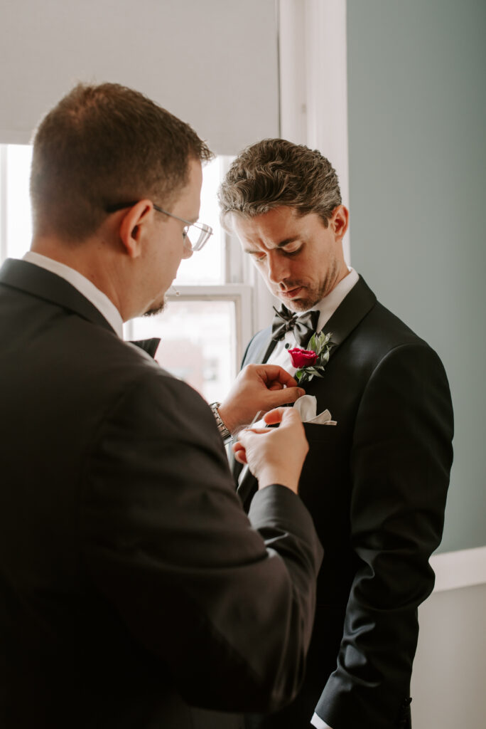 Groom getting boutonniere put on by groomsman