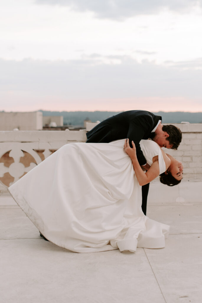Groom dipping bride on rooftop during sunset at Spokane Club