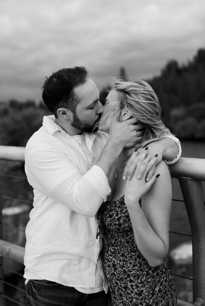 future bride and groom standing on bridge kissing while the wind is blowing