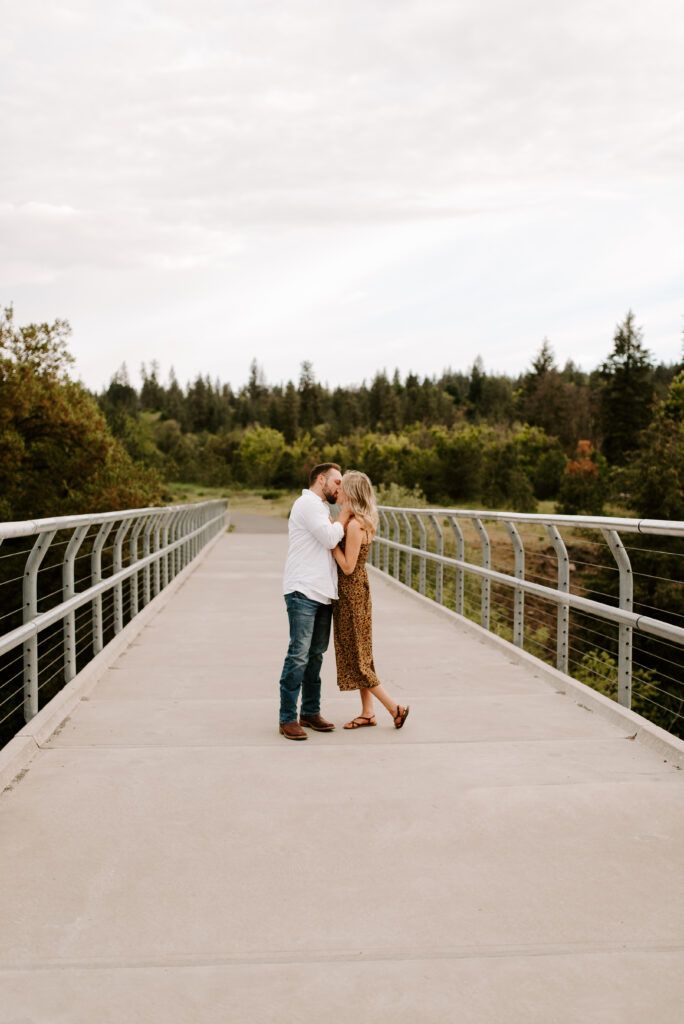 future bride and groom standing on bridge kissing