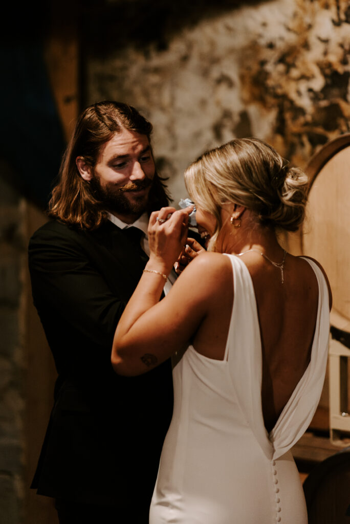 Aimee smiles and wipes her tears with a tissue with Johnny in the wine cellar of their wedding venue.